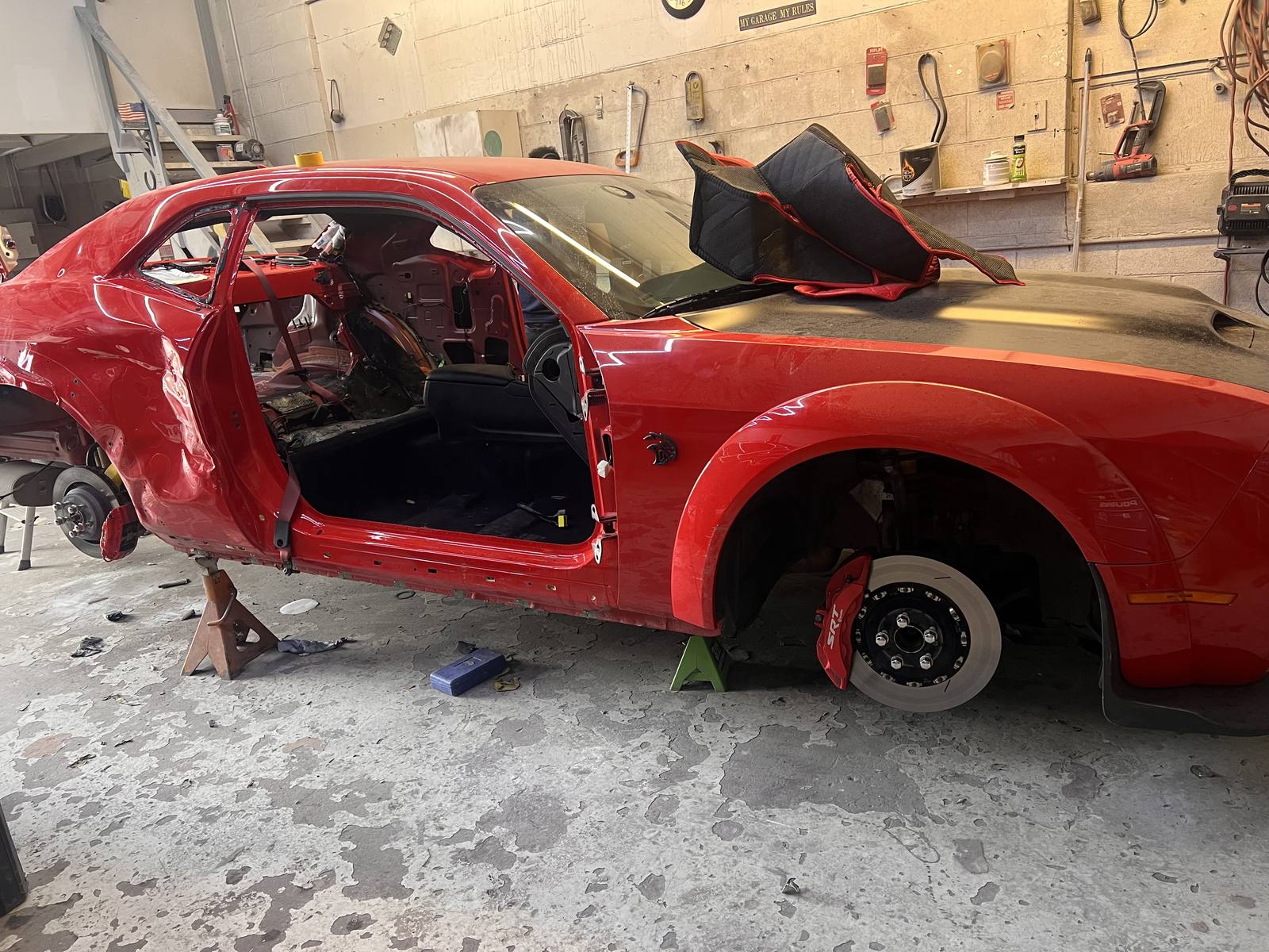 A red Dodge Challenger SRT with its doors removed and interior stripped, on jack stands mid-repair.