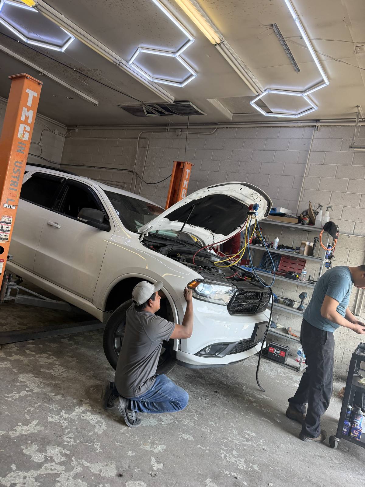 Two technicians working on a Dodge Durango in the bay, air conditioning gauges connected under the open hood.
