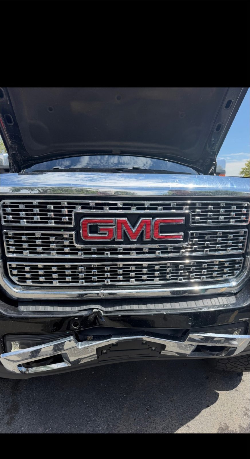 Black GMC Sierra Denali with the hood open and the lower front bumper crushed.