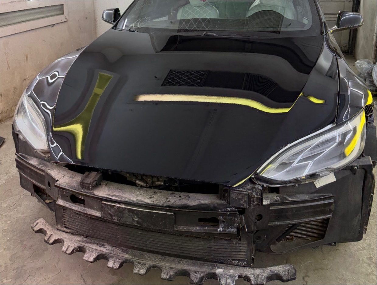 Tesla Model S with the front end removed down to the bare frame rail and radiator support, inside the shop.