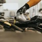 Close-up of a mechanic pouring engine oil into a car engine with gloved hands, indoors.