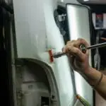 Close-up of vehicle dent repair in a garage using specialized tools under bright lighting.